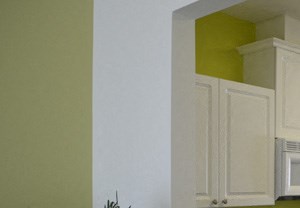 Opening with Black Countertops From Living Room Into Kitchen with White Cabinets, Standard Appliances and an Opening Through to Dining Room
